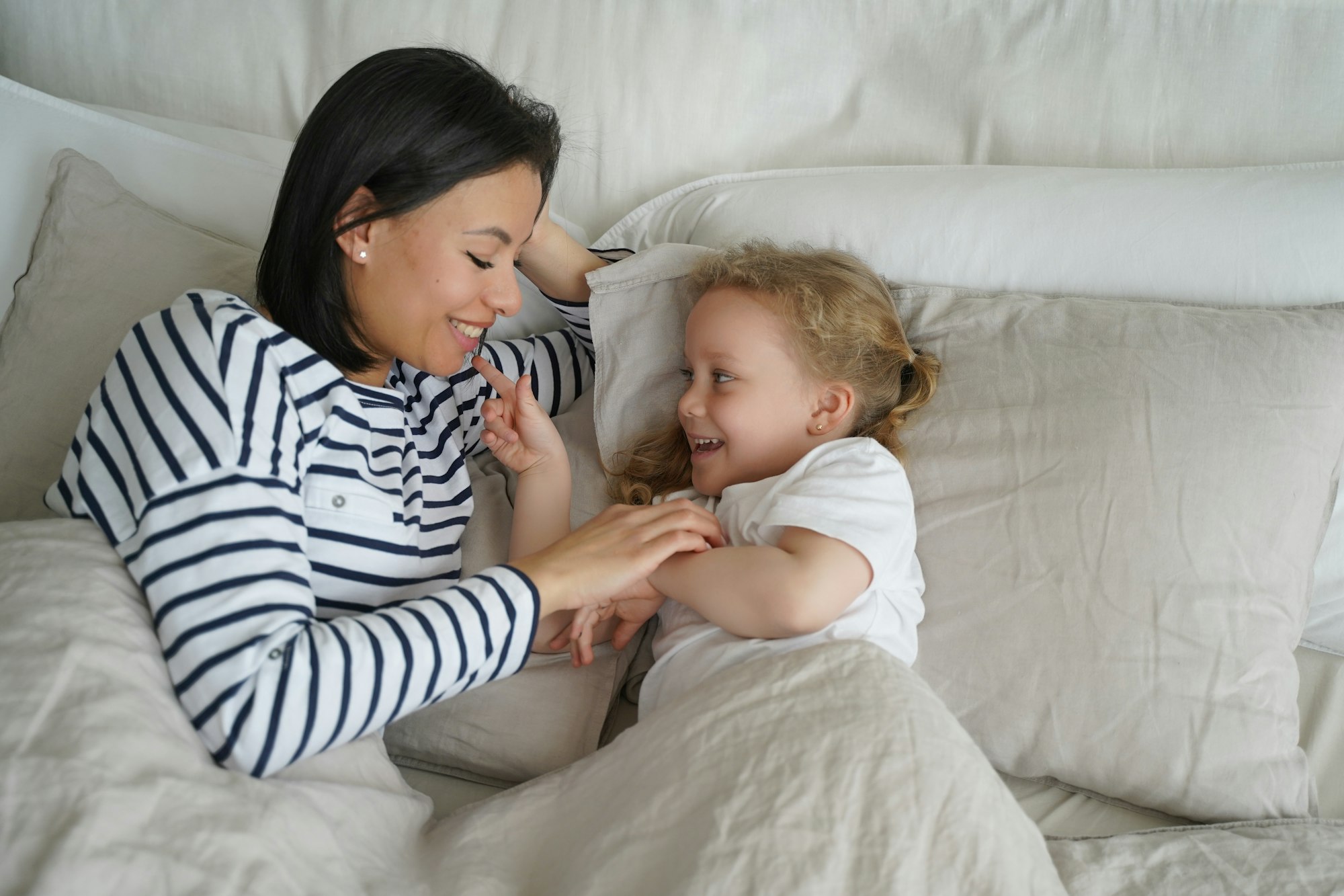 Mother and toddler daughter playing in bed, highlighting sleep apnea awareness in children. Sierra Sleep Airway and Wellness Center, Reno, NV.